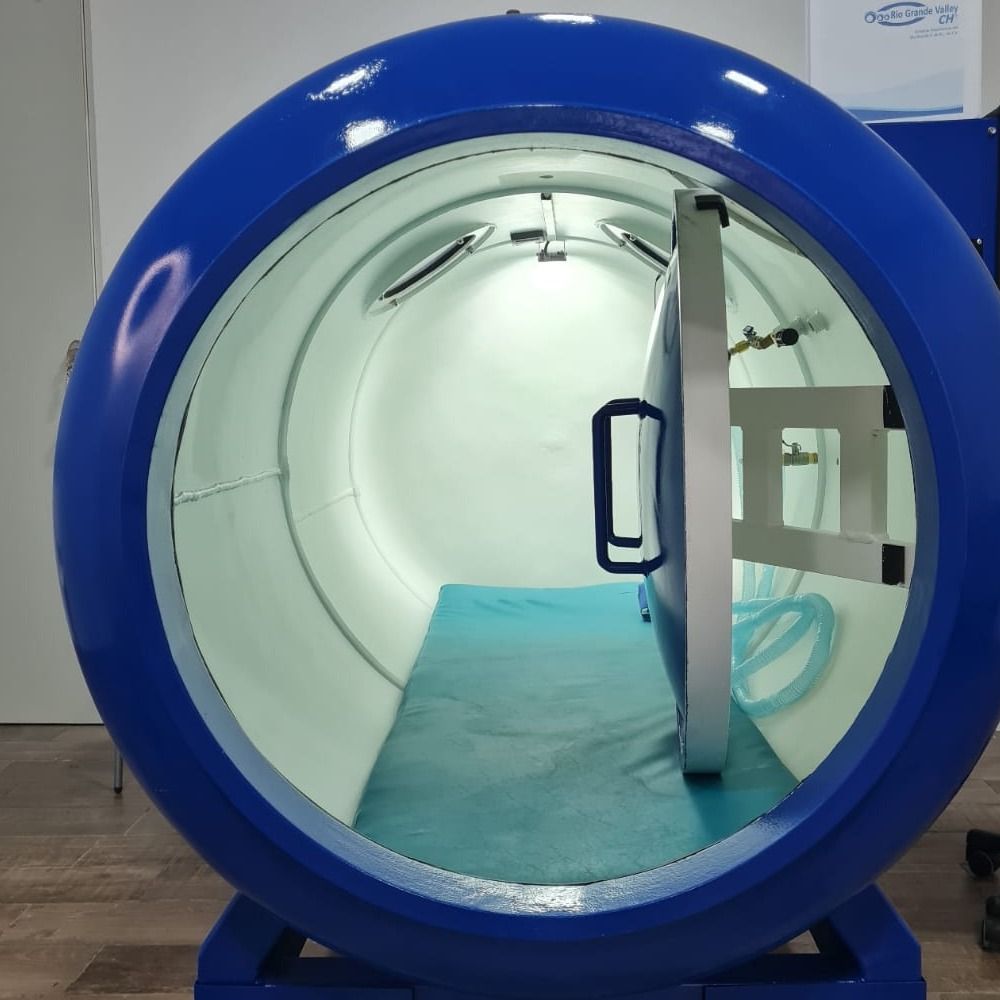 Cámara hiperbárica monoplaza azul vista de frente, con la escotilla abierta y la camilla al interior.